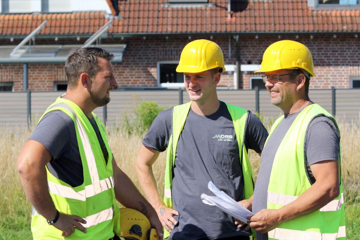 Drei Kollegen in Arbeitskleidung stehen zusammen und besprechen sich. 