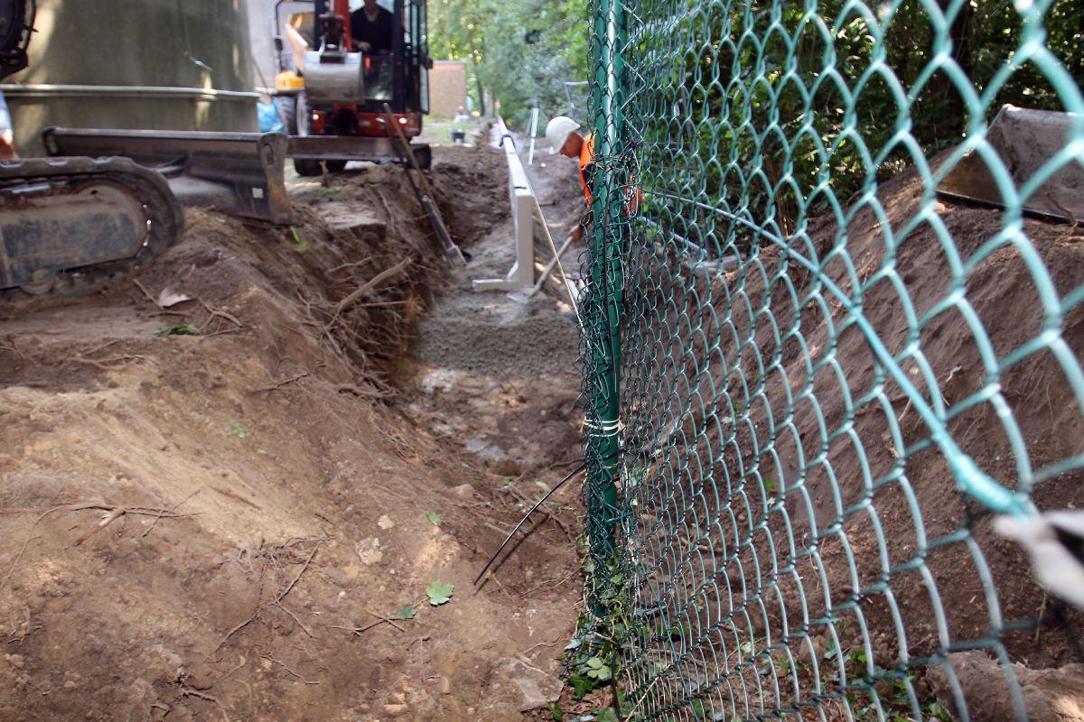 Auf der rechten Seite ist der alte Maschendrahtzaun zu sehen und weiter hinten im Bild die neuen Winkelstützwände. Deutlich werden die beengten Verhältnisse auf der Baustelle.