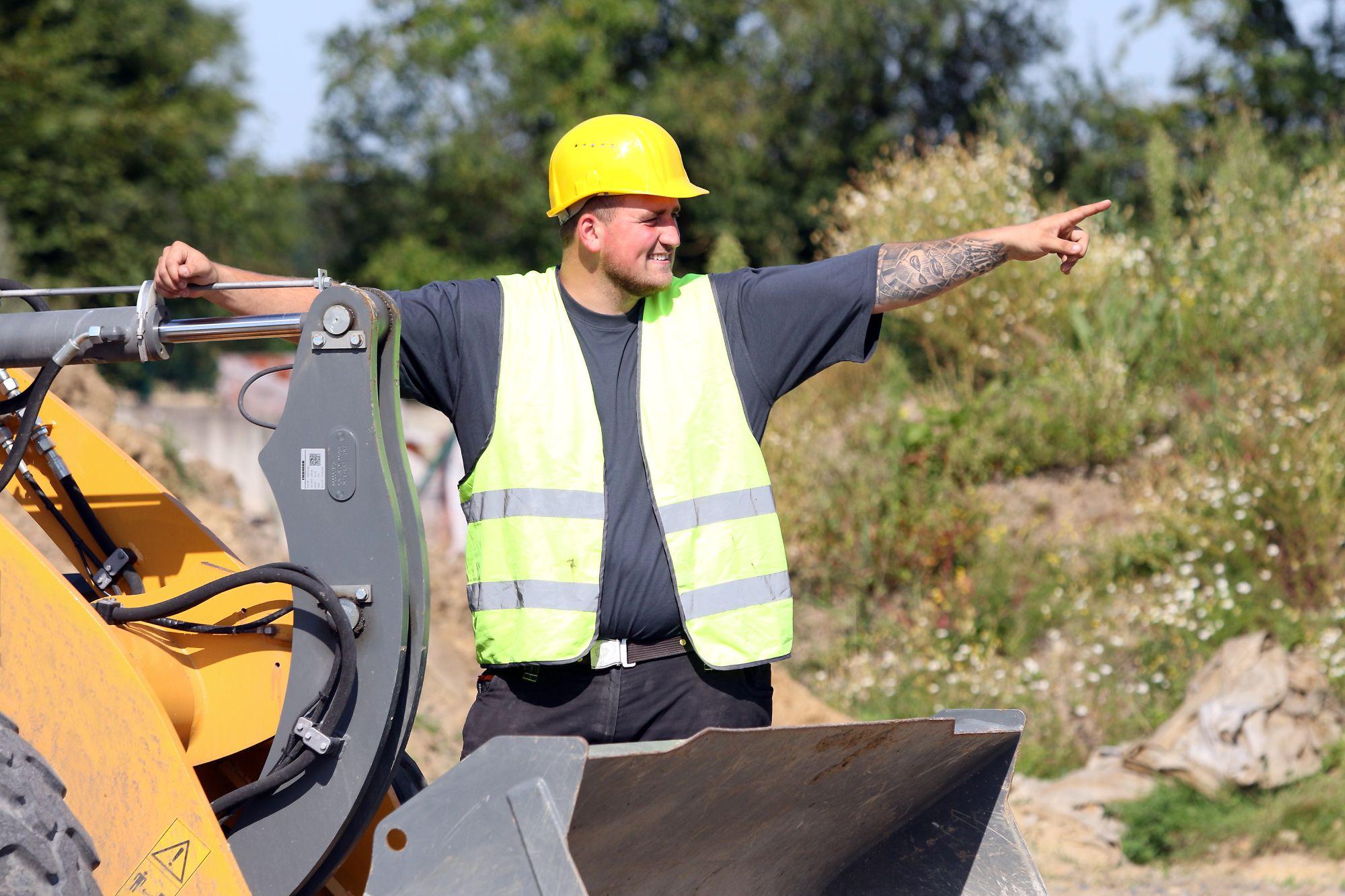 Bauarbeiter auf Baumaschine zeigt mit seinem Arm in eine Richtung.